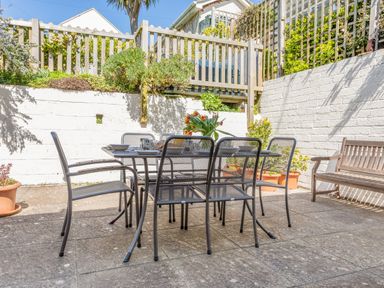 An outdoor patio with a metal dining table and six chairs a wooden bench and plants in pots at Cottage View in Hope Cove
