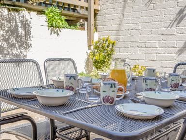 A metal outdoor table set with bowls mugs glasses a jug of orange juice and pastries in a garden at Cottage View in Hope Cove