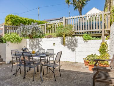 An outdoor patio with a metal table and six chairs a wooden bench potted plants and a small charcoal grill at Cottage View in Hope Cove