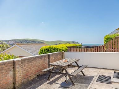 An outdoor patio area with a wooden picnic table and benches overlooking hills and the sea at Cottage View in Hope Cove