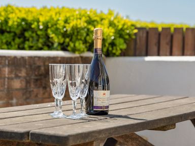 A bottle of prosecco and three empty glasses on a wooden outdoor table at Cottage View in Hope Cove