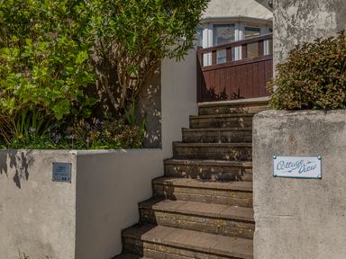 Stone steps leading up to a wooden gate and a house with plants on either side at Cottage View in Hope Cove