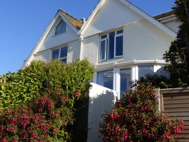 The exterior of a white house with triangular roof and multiple windows surrounded by bushes and flowers at Cottage View in Hope Cove