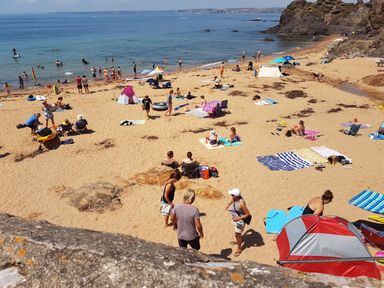 A sandy beach with people sunbathing swimming and sitting under umbrellas near rocky cliffs at Cottage View in Hope Cove