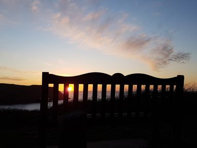 A wooden bench overlooking a coastline at sunset at Cottage View in Hope Cove
