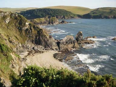 A rocky coastline with a sandy beach and green hills in the background at Cottage View in Hope Cove