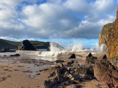 A beach with rocks and a sea wall with waves crashing at Cottage View in Hope Cove