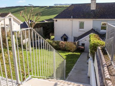 An outdoor view of a pathway with metal railings leading to a house with a sloped roof and garden area at Cottage View in Hope Cove