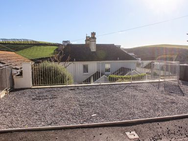 A gravel terrace with metal railings overlooking rooftops and green hills at Cottage View in Hope Cove