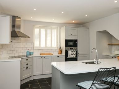 A kitchen with gray cabinets white countertop and a window with shutters at Cindy's Retreat in Hope Cove