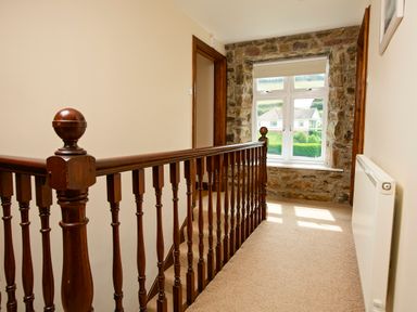 A hallway with wooden banister carpeted floor and window with stone frame at Cindy's Retreat in Hope Cove