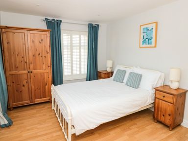 A bedroom with a double bed two wooden bedside cabinets a wooden wardrobe and blue curtains at Cindys Retreat in Hope Cove