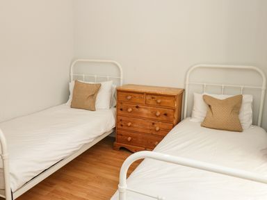 A bedroom with two single beds with white frames and bedding and a wooden chest of drawers between the beds at Cindys Retreat in Hope Cove