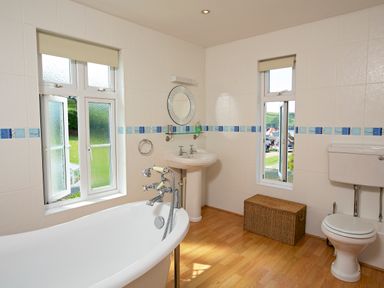 A bathroom with a bathtub sink toilet wicker storage box and two windows at Cindys Retreat in Hope Cove