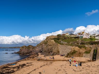A sandy beach with people and rocky cliffs with houses on top at Cindy's Retreat in Hope Cove