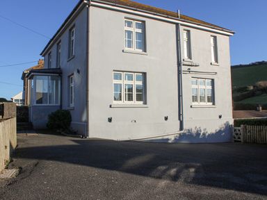 The exterior of a two-story house with white walls and multiple windows next to a paved driveway at Cindy's Retreat in Hope Cove