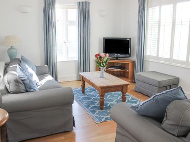 A living room with grey sofas a wooden coffee table with flowers a television and blue patterned rug at Cindys Retreat in Hope Cove