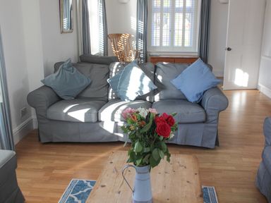 A living room with a grey sofa and blue cushions a wooden table with flowers and a rocking chair at Cindys Retreat in Hope Cove