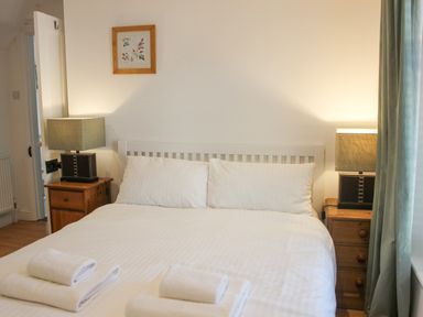 A bedroom with a double bed white bedding bedside tables lamps and folded towels at Cindys Retreat in Hope Cove