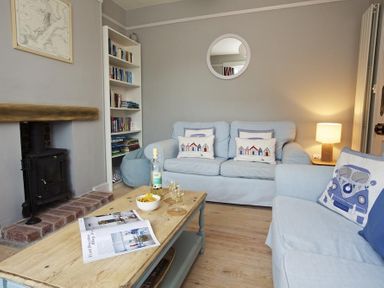 A living room with light blue sofas a wooden coffee table a bookshelf and a wood burning stove at Crab Cottage in Salcombe