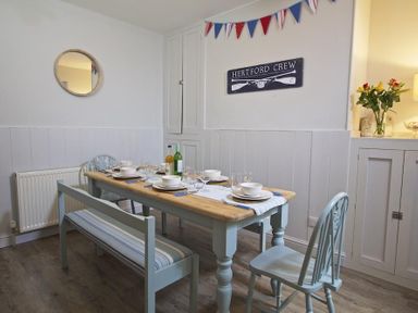 A dining room with a wooden table set with dishes and glasses and light blue chairs at Crab Cottage in Salcombe