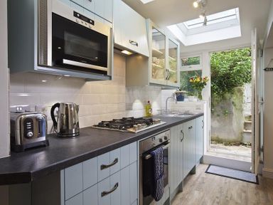 A kitchen with countertop appliances gas stove oven sink and a door leading outside at Crab Cottage in Salcombe