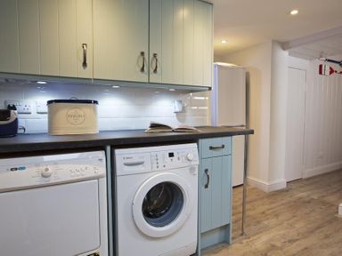 A laundry room with washing machine, dryer, cabinets, countertop, and refrigerator at Crab Cottage Salcombe