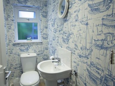 A small bathroom with a toilet sink and round mirror with patterned walls at Crab Cottage in Salcombe