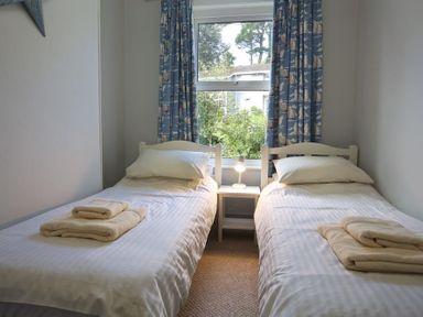 A bedroom with two single beds towels on beds and a window with blue curtains at Crab Cottage in Salcombe