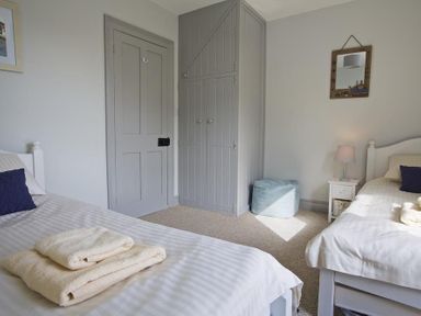 A bedroom with two single beds a nightstand with a lamp a built-in wardrobe and a door at Crab Cottage in Salcombe