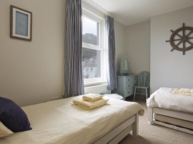A bedroom with two beds a dresser with mirror a chair and a window with striped curtains at Crab Cottage in Salcombe