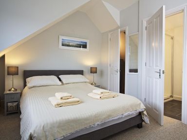 A bedroom with a double bed two bedside tables with lamps folded towels on the bed and an open door leading to a bathroom at Crab Cottage in Salcombe