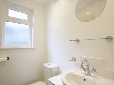 A bathroom with a window toilet sink faucet mirror and glass shelf at Crab Cottage in Salcombe