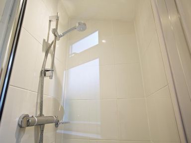 A shower head and controls in a tiled shower at Crab Cottage in Salcombe