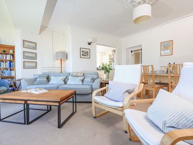 A living room with a blue sofa white armchairs wooden coffee tables a dining table and chairs at Edinburgh House in Salcombe