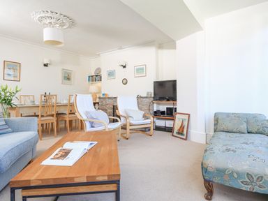 A living room with a wooden coffee table two armchairs a blue sofa a floral chaise lounge a dining table with chairs and a television at Edinburgh House in Salcombe
