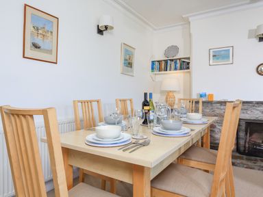 A dining room with a wooden table set with plates bowls glasses and cutlery by a stone fireplace at Edinburgh House in Salcombe