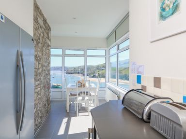 A kitchen with a dining table set near large windows overlooking a beach and hills at Edinburgh House in Salcombe