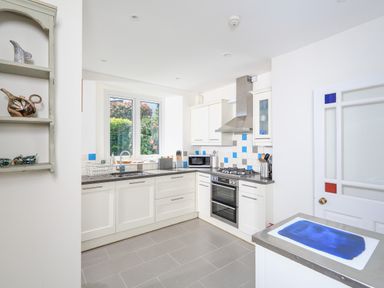 A kitchen with white cabinets a window above the sink and a stove with an oven at Edinburgh House in Salcombe