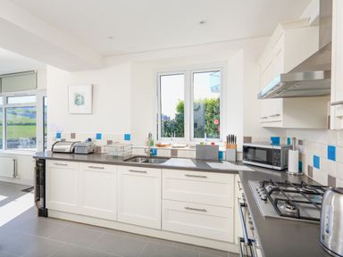 A kitchen with a gas stove microwave toaster and dishwasher under a window at Edinburgh House in Salcombe