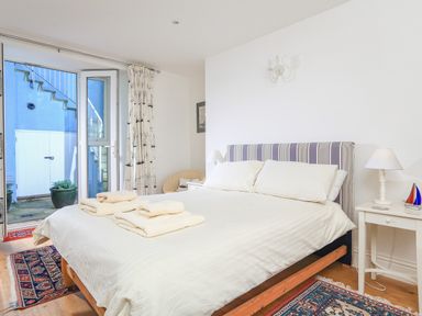 A bedroom with a bed with folded towels on it a chair bedside tables and open doors leading outside at Edinburgh House in Salcombe