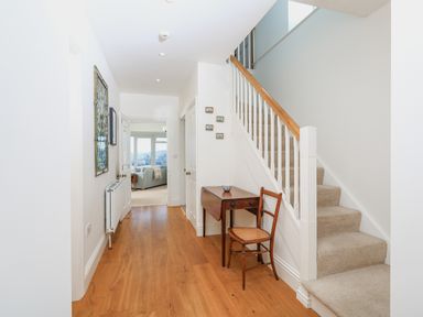A hallway with wooden floor a staircase and a wooden table with a chair at Edinburgh House in Salcombe