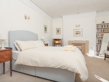 A bedroom with a bed bedside tables lamps a fireplace bookshelf and a standing mirror at Edinburgh House in Salcombe