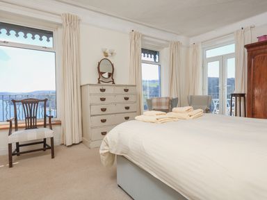 A bedroom with a bed a chest of drawers two chairs and large windows showing a view at Edinburgh House in Salcombe