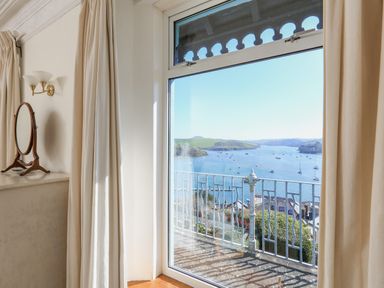 A window with cream curtains overlooking a balcony and a water view at Edinburgh House in Salcombe