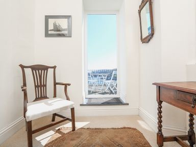 A room with a wooden chair and table a framed picture on the wall and a door leading to a balcony with white outdoor furniture at Edinburgh House in Salcombe