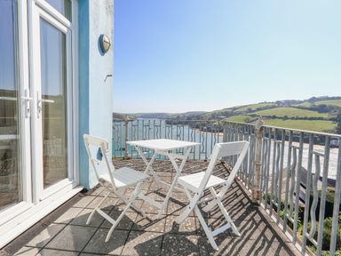 A balcony with a white table and chairs overlooking a river and green hills at Edinburgh House in Salcombe