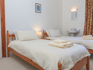 A bedroom with two single beds wooden frames bedside table with lamp and a wall-mounted sink at Edinburgh House in Salcombe