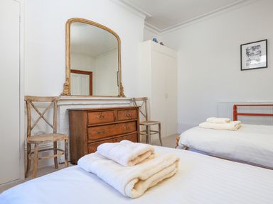 A bedroom with two single beds towels on beds wooden chest of drawers large mirror two chairs wardrobe and framed picture at Edinburgh House in Salcombe