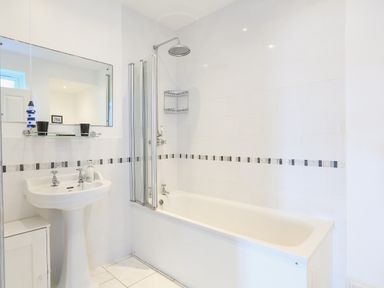 A bathroom with a bathtub shower combination a pedestal sink and a mirror at Edinburgh House in Salcombe